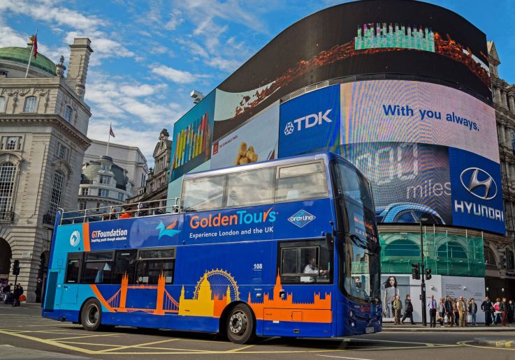 Autobús turístico de dos pisos frente a las pantallas luminosas de Piccadilly Circus.
