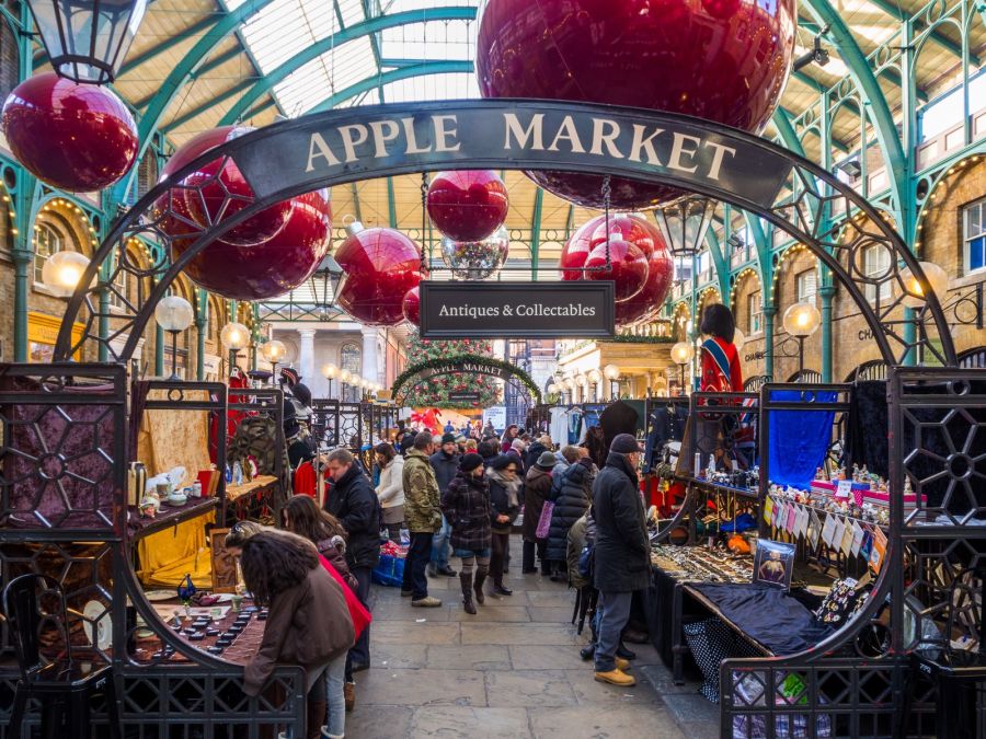 Grandes bolas rojas colgadas bajo la cubierta del Apple Market de Covent Garden, sobre los puestos y los visitantes