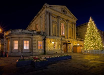Un edificio histórico de Bath iluminado junto a un gran árbol de Navidad.