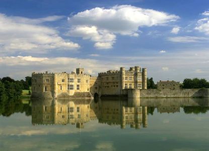 El Castillo de Leeds reflejado en el lago que lo rodea, bajo un cielo de nubes blancas.