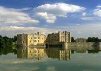 El Castillo de Leeds reflejado en el lago que lo rodea, bajo un cielo de nubes blancas.