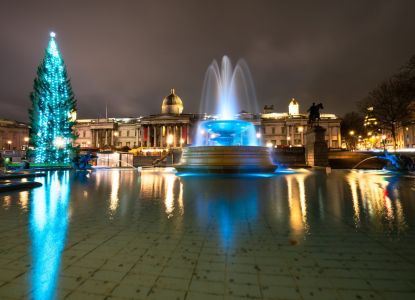 El árbol de Navidad de Trafalgar Square iluminado junto a las fuentes al anochecer.