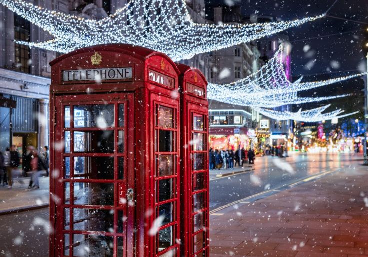 Cabina telefónica roja bajo las luces navideñas mientras nieva.