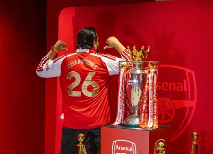 Visitante con camiseta del Arsenal junto al trofeo de la Premier League en el Emirates Stadium