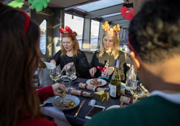 Comensales con diademas navideñas disfrutando del almuerzo mientras el barco navega.
