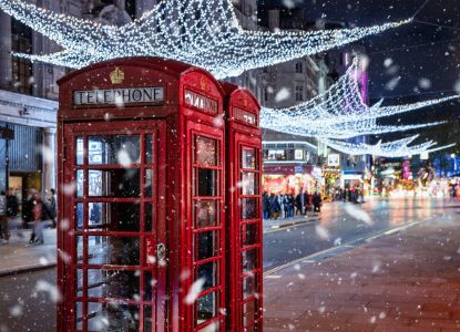 Cabina telefónica roja bajo las luces navideñas mientras nieva.