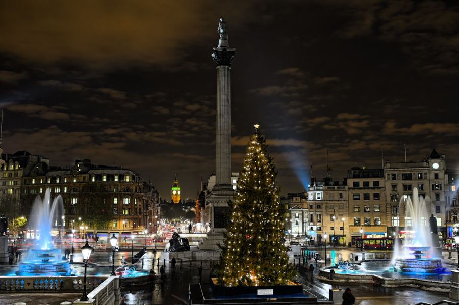 Árbol de Navidad iluminado y fuentes encendidas en Trafalgar Square de noche, al pie de la columna de Nelson