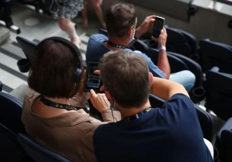 Visitantes con dispositivo multimedia en las gradas del Tottenham Hotspur Stadium