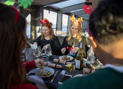 Comensales con diademas navideñas disfrutando del almuerzo mientras el barco navega.