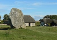 Un megalito del círculo de Avebury junto a una casa con tejado de paja del pueblo.